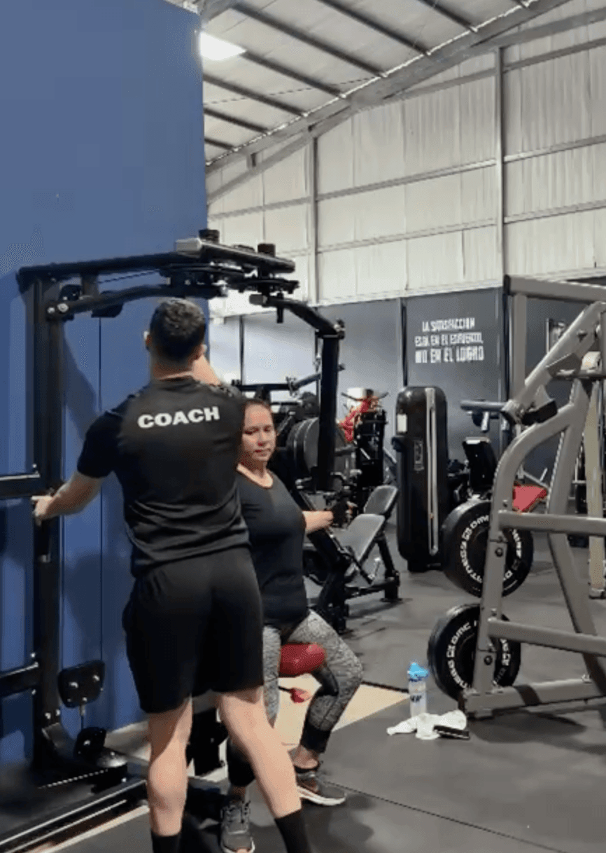 Gym trainer assisting a woman using exercise equipment in a fitness center.